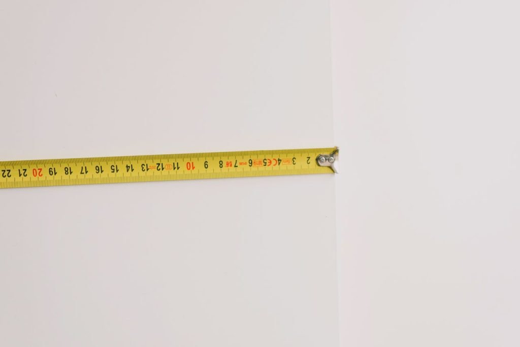 Minimalist image of a yellow measuring tape extended across a white wall, showcasing DIY precision.